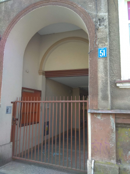 Zdjęcie przedstawia dużą  bramę wejściową do budynku, w krórym  znajduje się lokal mieszkalny na sprzedaż.